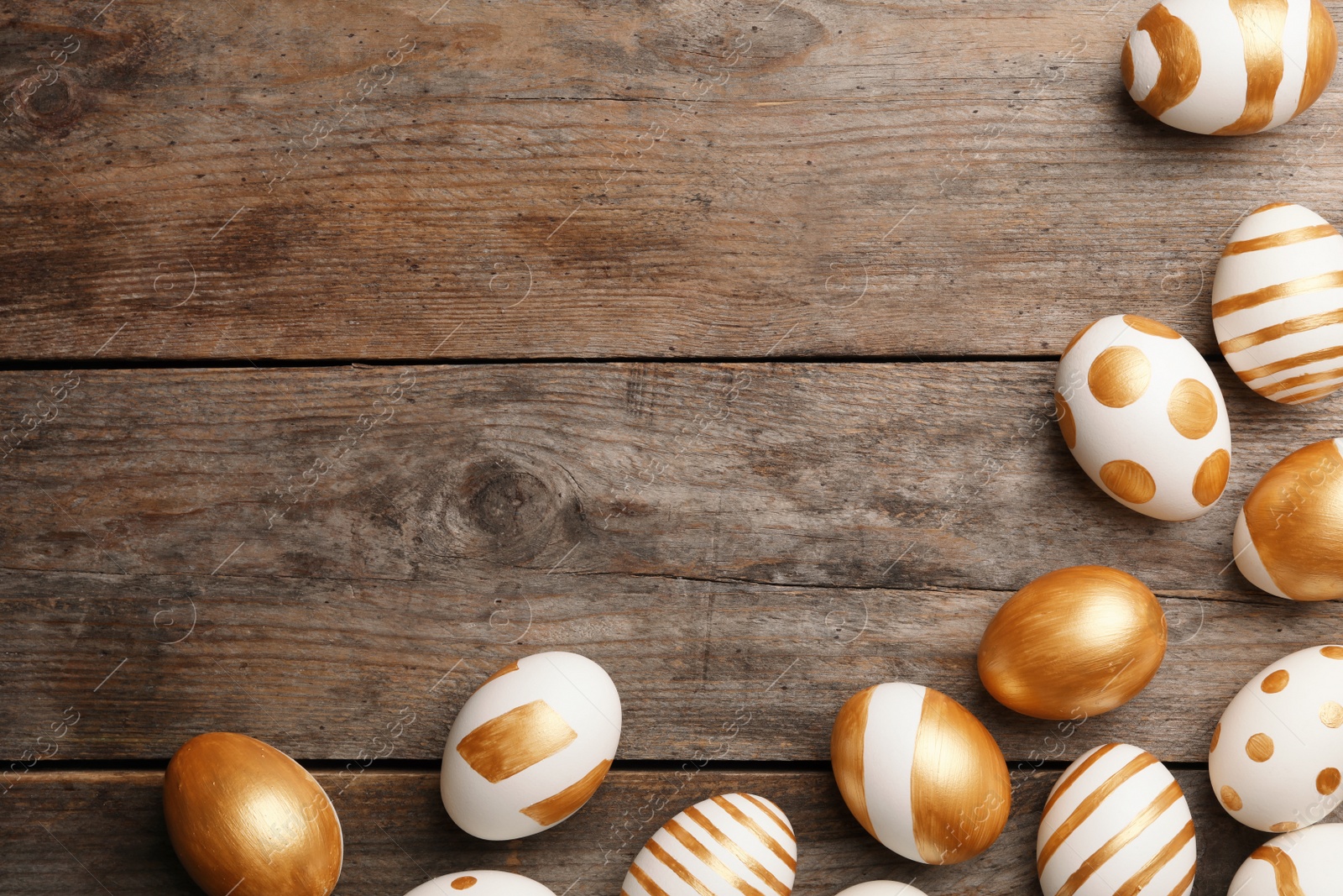 Photo of Flat lay composition of traditional Easter eggs decorated with golden paint on wooden background, space for text