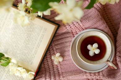 Open book, cup of aromatic tea and beautiful jasmine flowers on pink fabric, flat lay