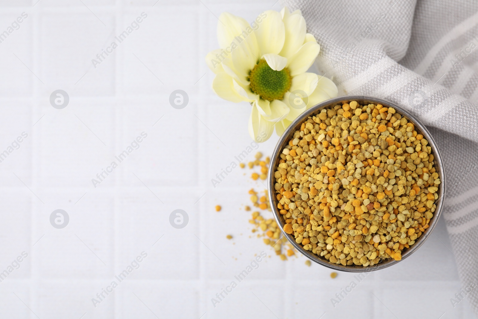 Photo of Fresh bee pollen granules and flower on white table, top view. Space for text