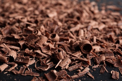 Photo of Pile of tasty chocolate curls on black background, closeup