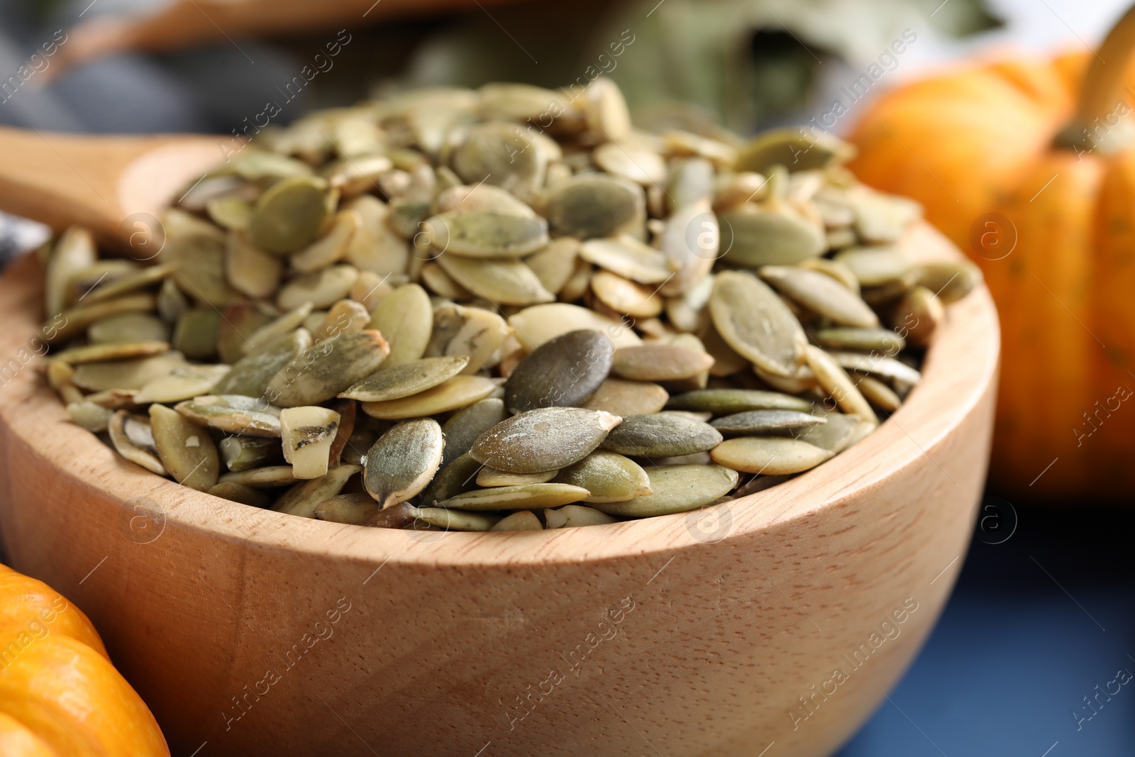 Photo of Wooden bowl with pumpkin seeds on blue table, closeup