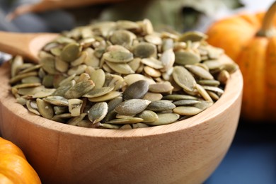 Wooden bowl with pumpkin seeds on blue table, closeup