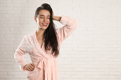 Young woman in bathrobe with wet hair near white brick wall. Space for text