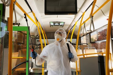 Photo of Public transport sanitation. Worker in protective suit disinfecting bus salon