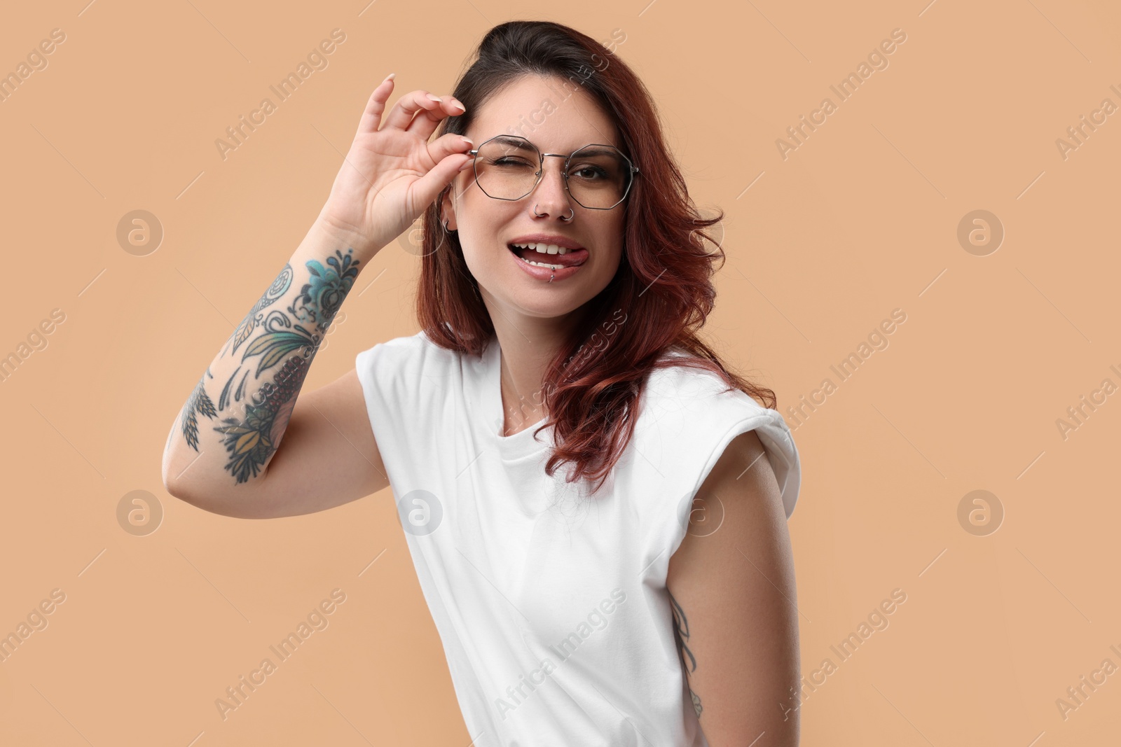 Photo of Beautiful tattooed woman showing her tongue on beige background