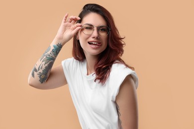 Photo of Beautiful tattooed woman showing her tongue on beige background
