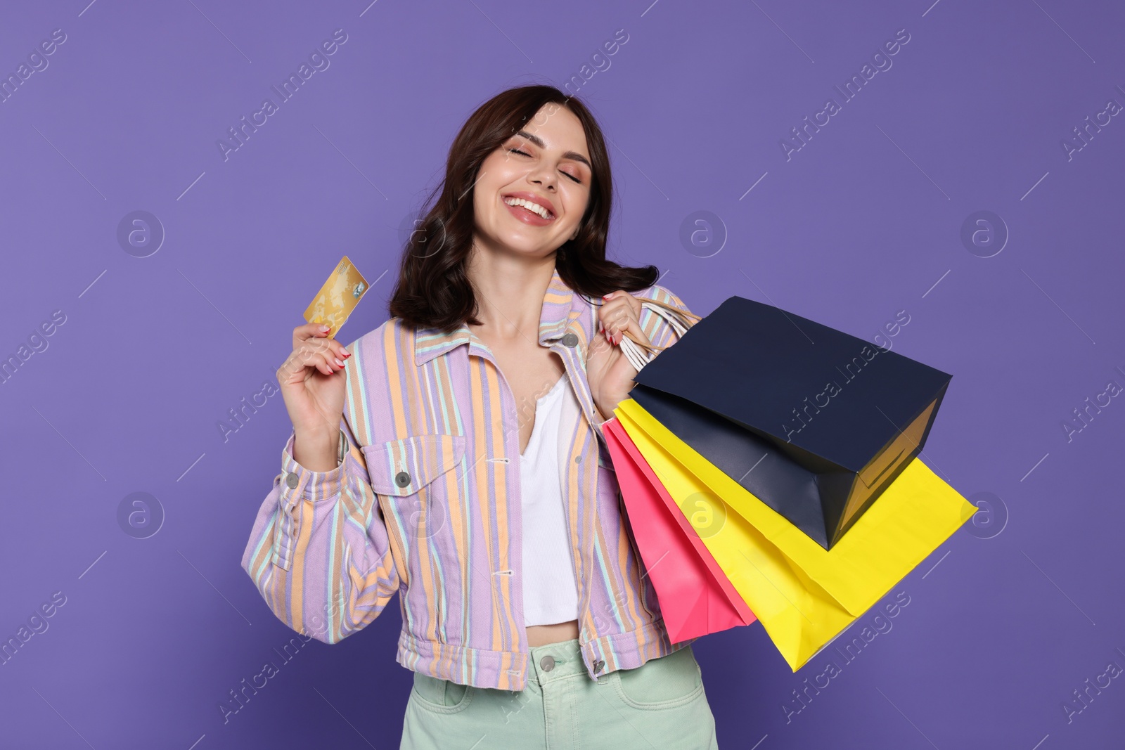 Photo of Beautiful young woman with paper shopping bags and credit card on purple background