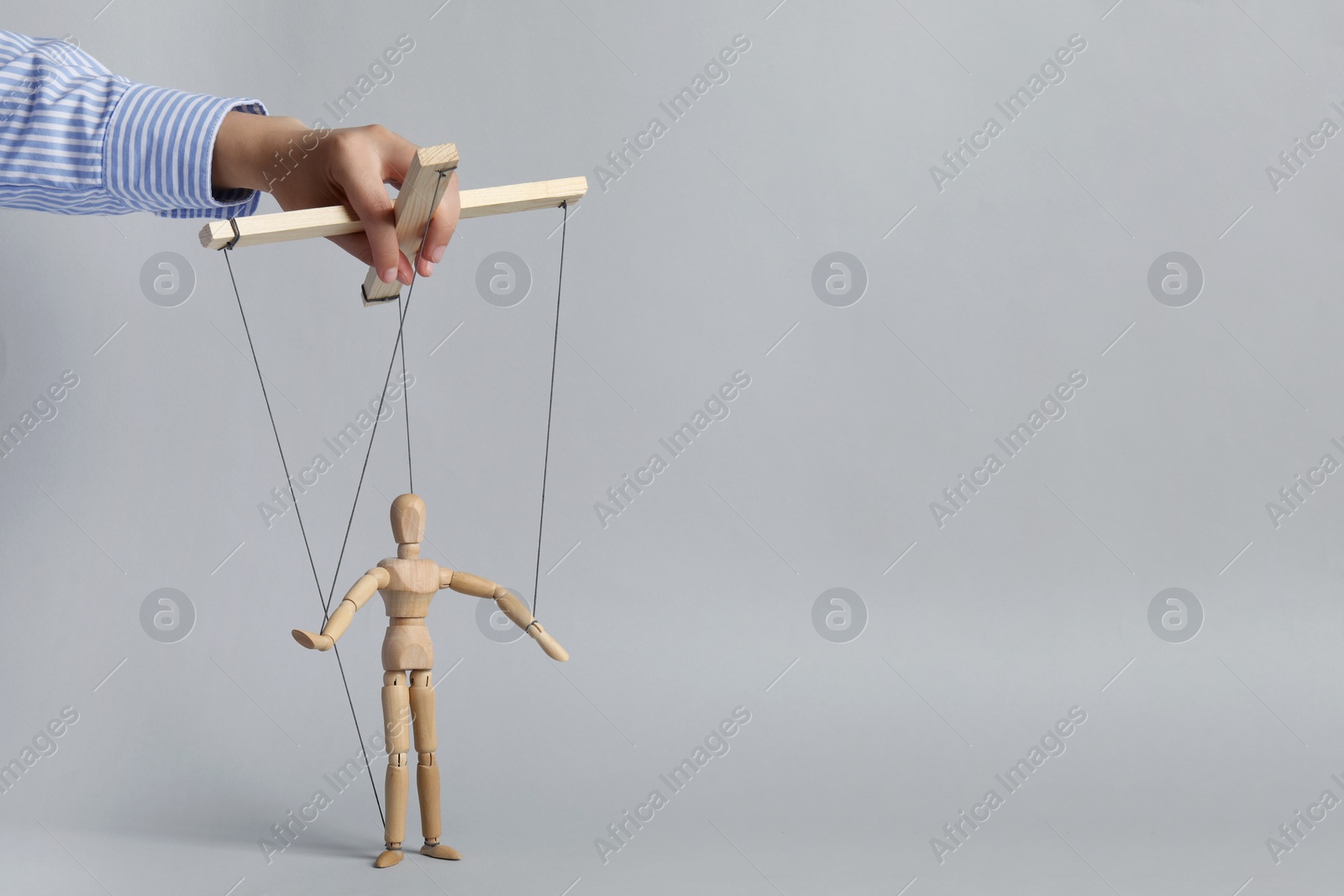 Photo of Woman pulling strings of puppet on light grey background, closeup. Space for text