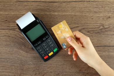 Woman with credit card using modern payment terminal at wooden table, top view