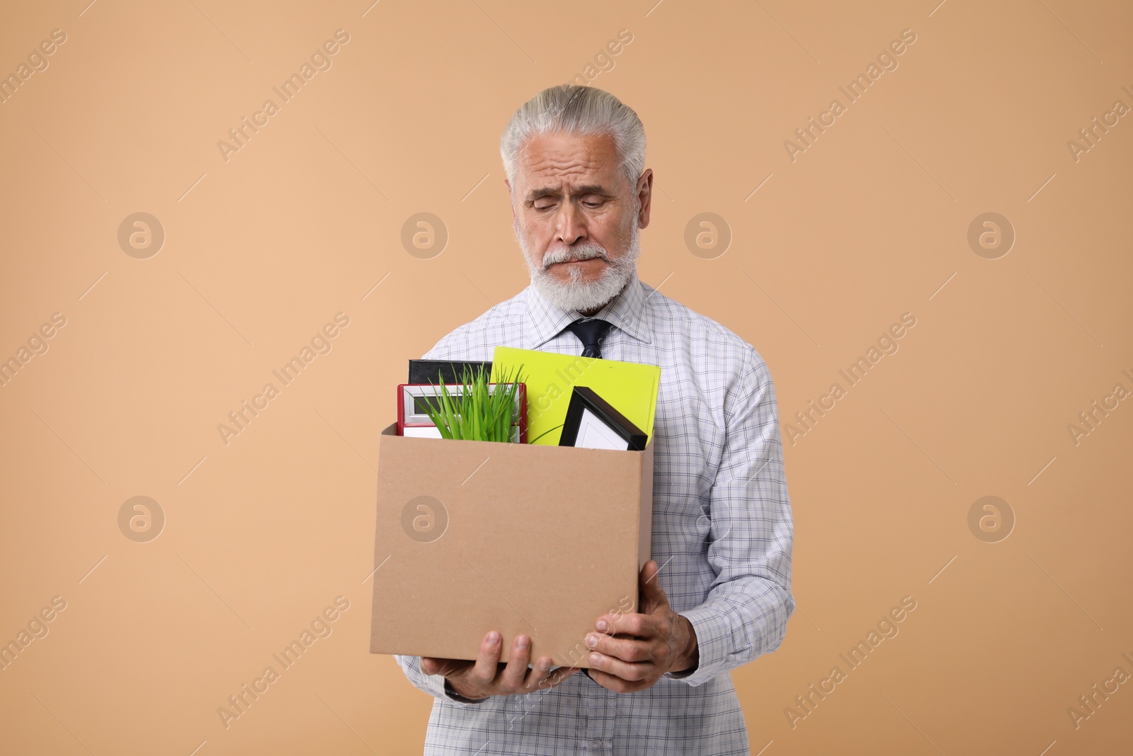 Photo of Unemployed senior man with box of personal office belongings on beige background