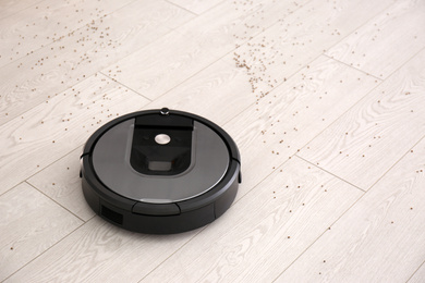 Photo of Modern robotic vacuum cleaner removing scattered buckwheat from wooden floor. Space for text