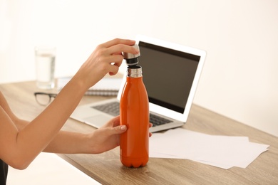 Woman with orange thermos bottle at workplace, closeup
