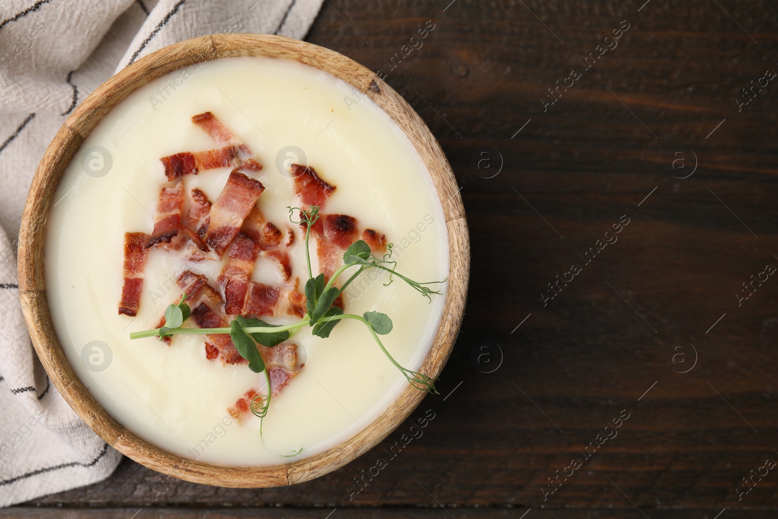 Photo of Delicious potato soup with bacon and microgreens in bowl on wooden table, top view. Space for text