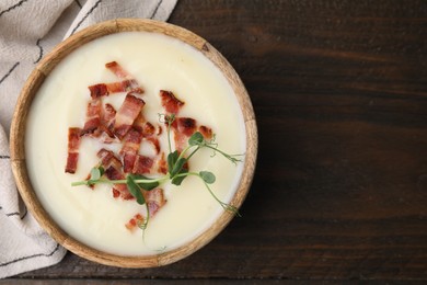 Photo of Delicious potato soup with bacon and microgreens in bowl on wooden table, top view. Space for text