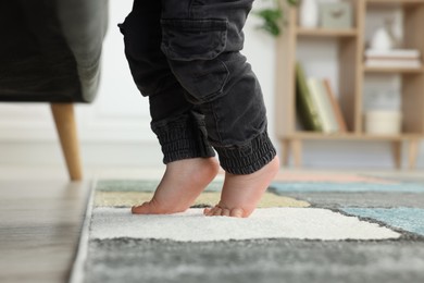 Photo of Baby standing on soft carpet near sofa, closeup