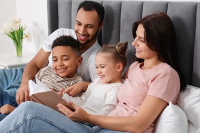 Photo of Happy international family reading book on bed