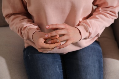 Woman taking off wedding ring on sofa, closeup. Divorce concept