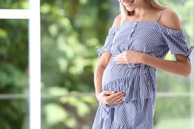 Happy pregnant woman standing near window at home