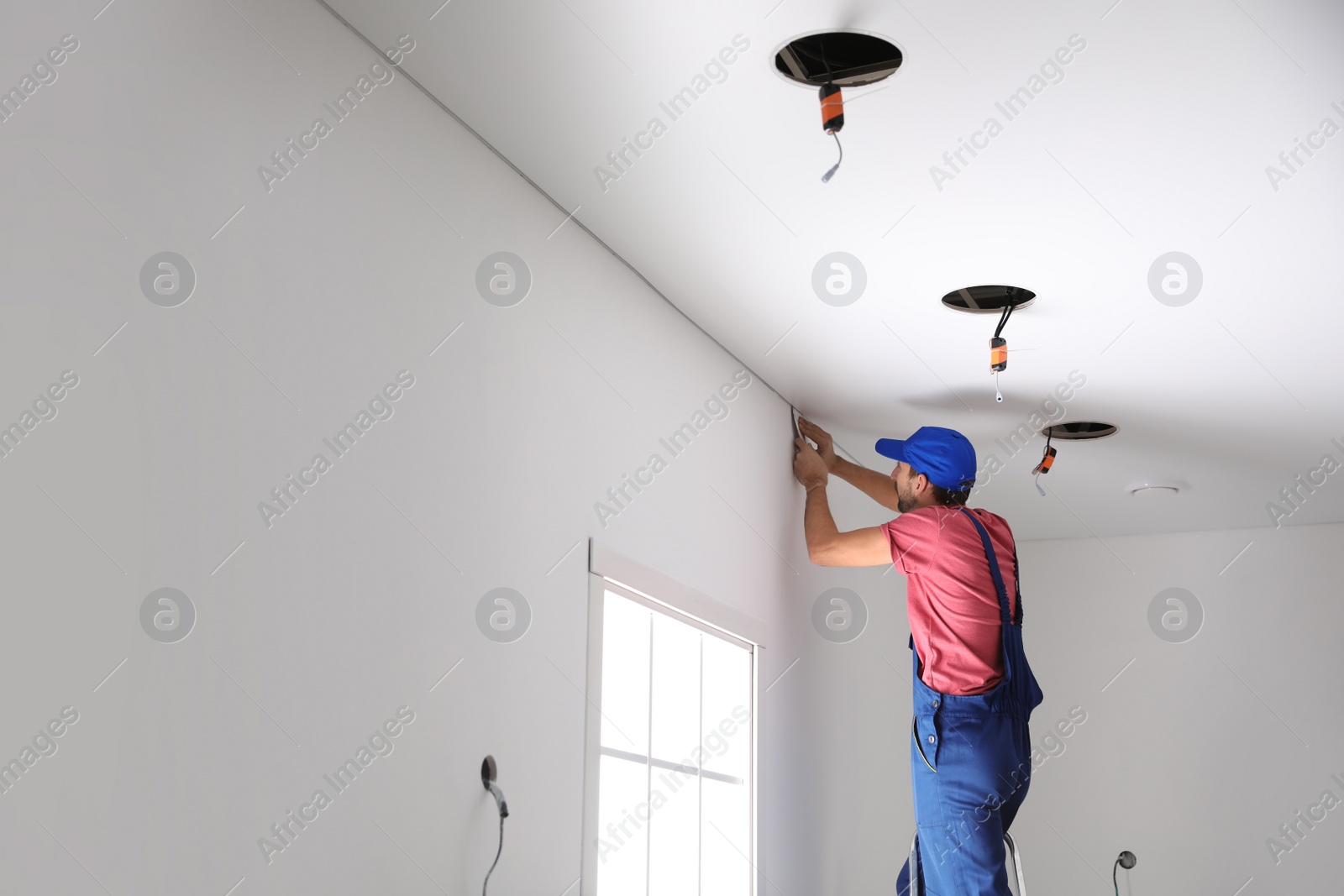 Photo of Worker installing stretch ceiling in empty room. Space for text