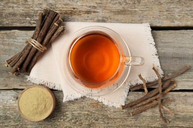 Aromatic licorice tea in cup, dried sticks of licorice root and powder on wooden table, flat lay