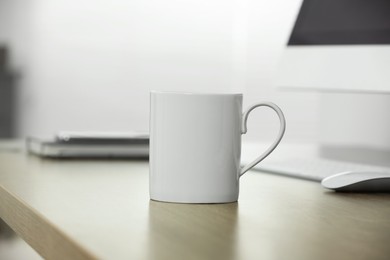 Photo of White ceramic mug on wooden table at workplace. Mockup for design