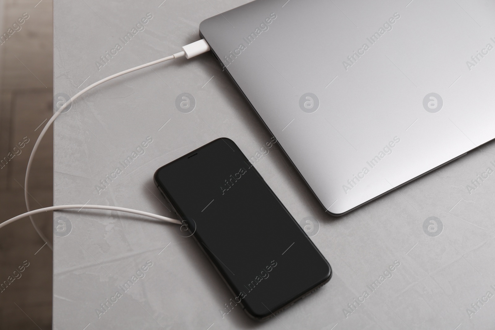 Photo of Smartphone with wireless charger connected to laptop on light grey table, above view. space for text