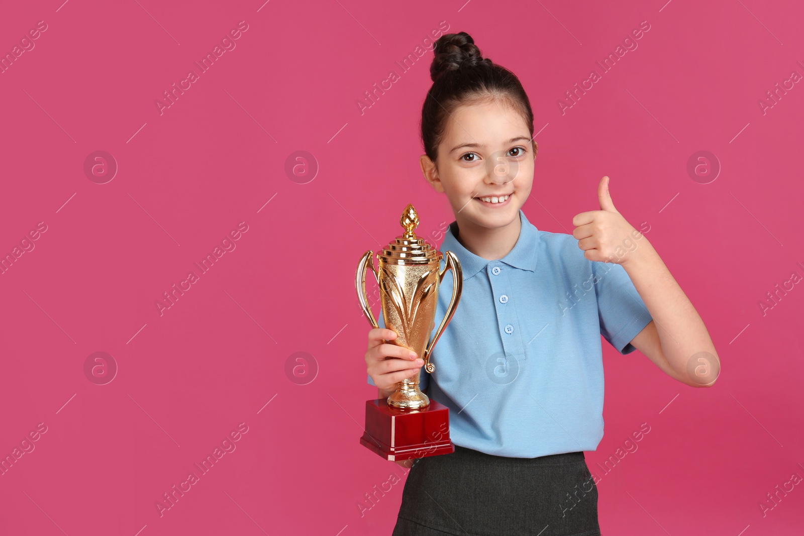 Photo of Happy girl in school uniform with golden winning cup on pink background. Space for text