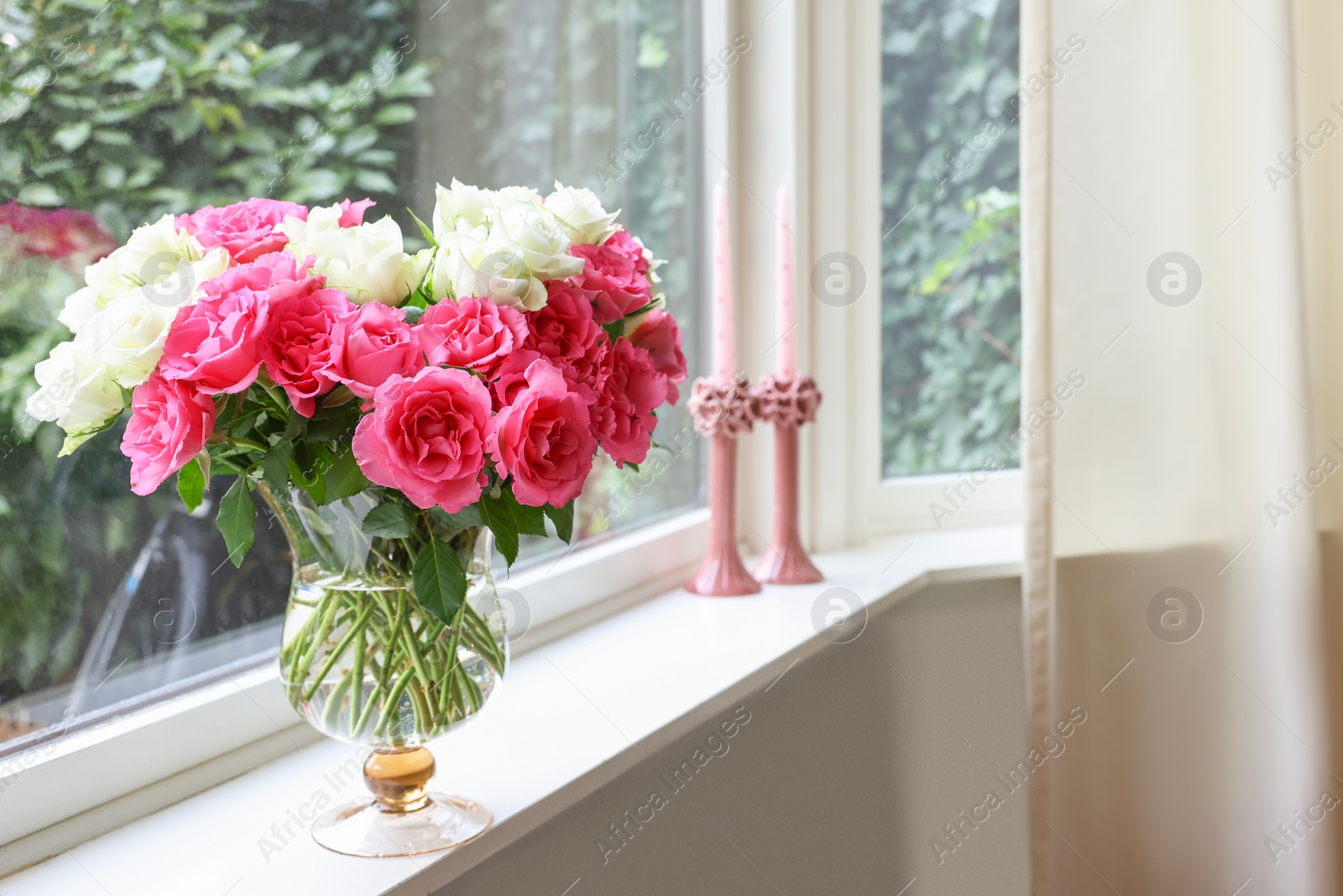 Photo of Vase with beautiful bouquet of roses and candles on windowsill indoors, space for text