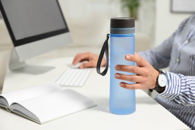 Man taking transparent plastic bottle of water while working on computer in office, closeup