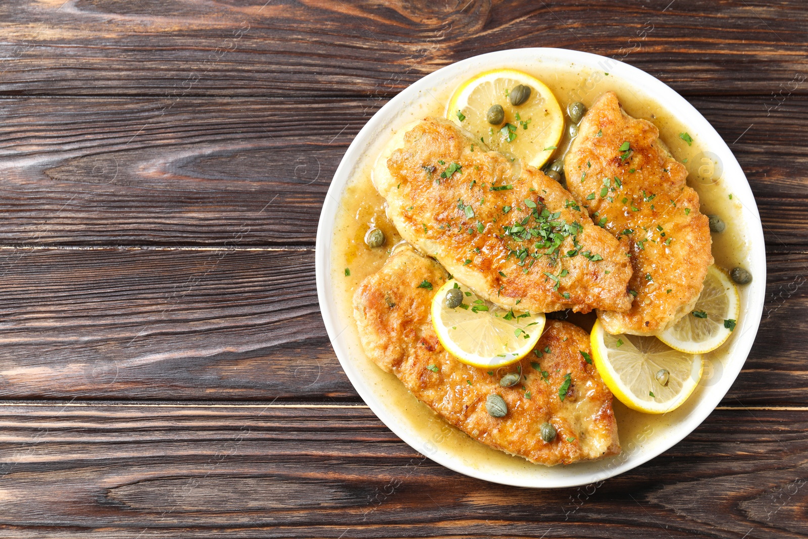 Photo of Delicious chicken piccata on wooden table, top view. Space for text