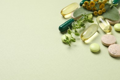 Photo of Different pills and herbs on light green background, space for text. Dietary supplements