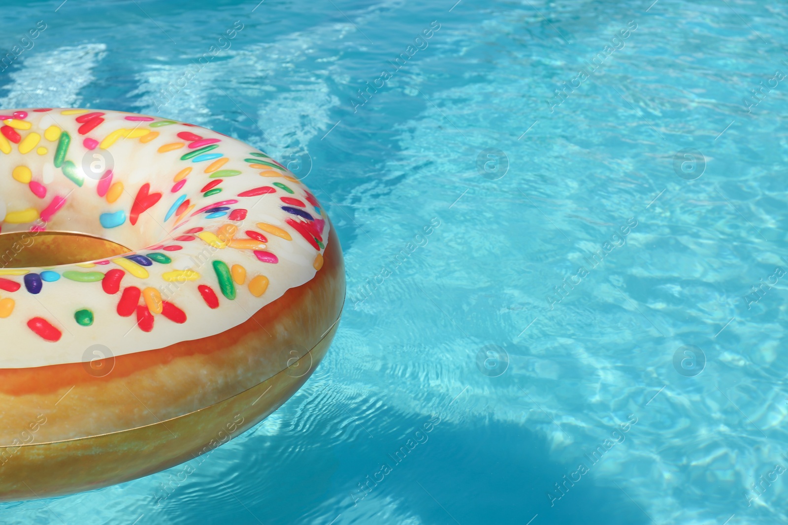 Photo of Bright inflatable doughnut ring floating in swimming pool on sunny day. Space for text