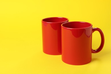 Two red ceramic mugs on yellow background. Space for text