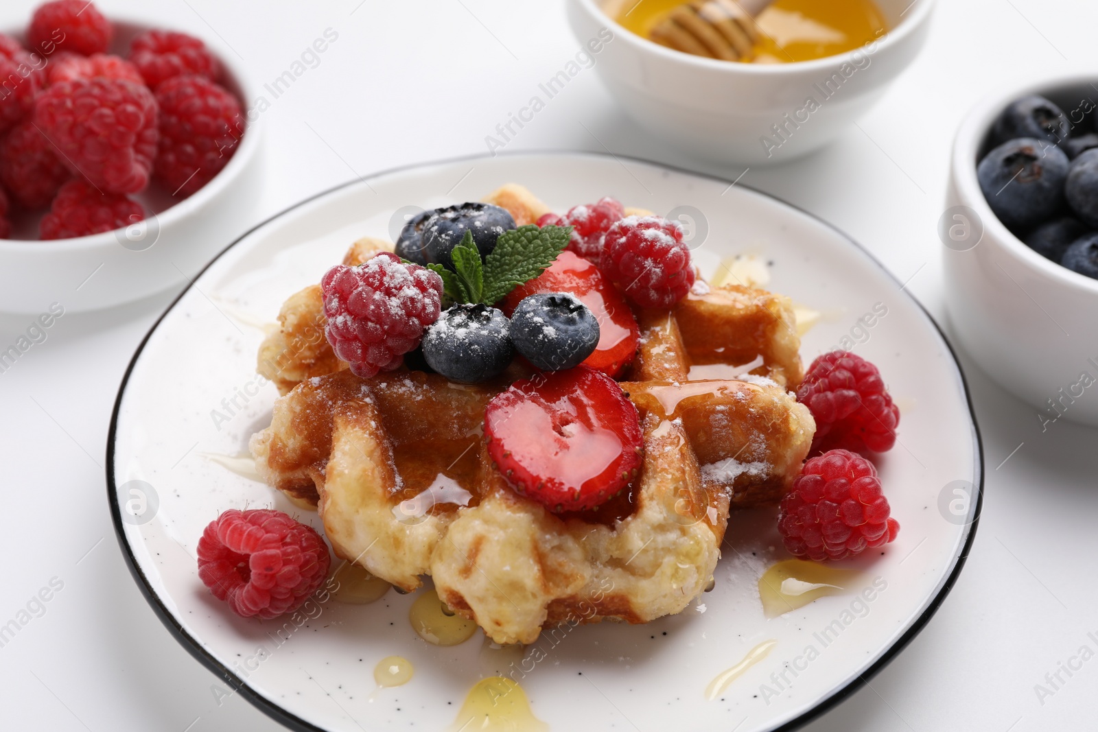 Photo of Delicious Belgian waffle with fresh berries and honey on white table, closeup