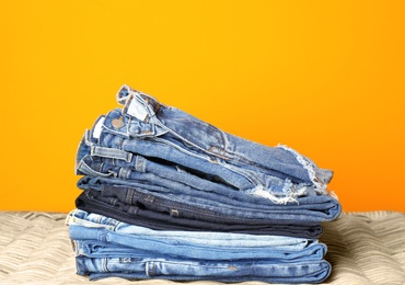 Photo of Stack of jeans on wicker chest against color background