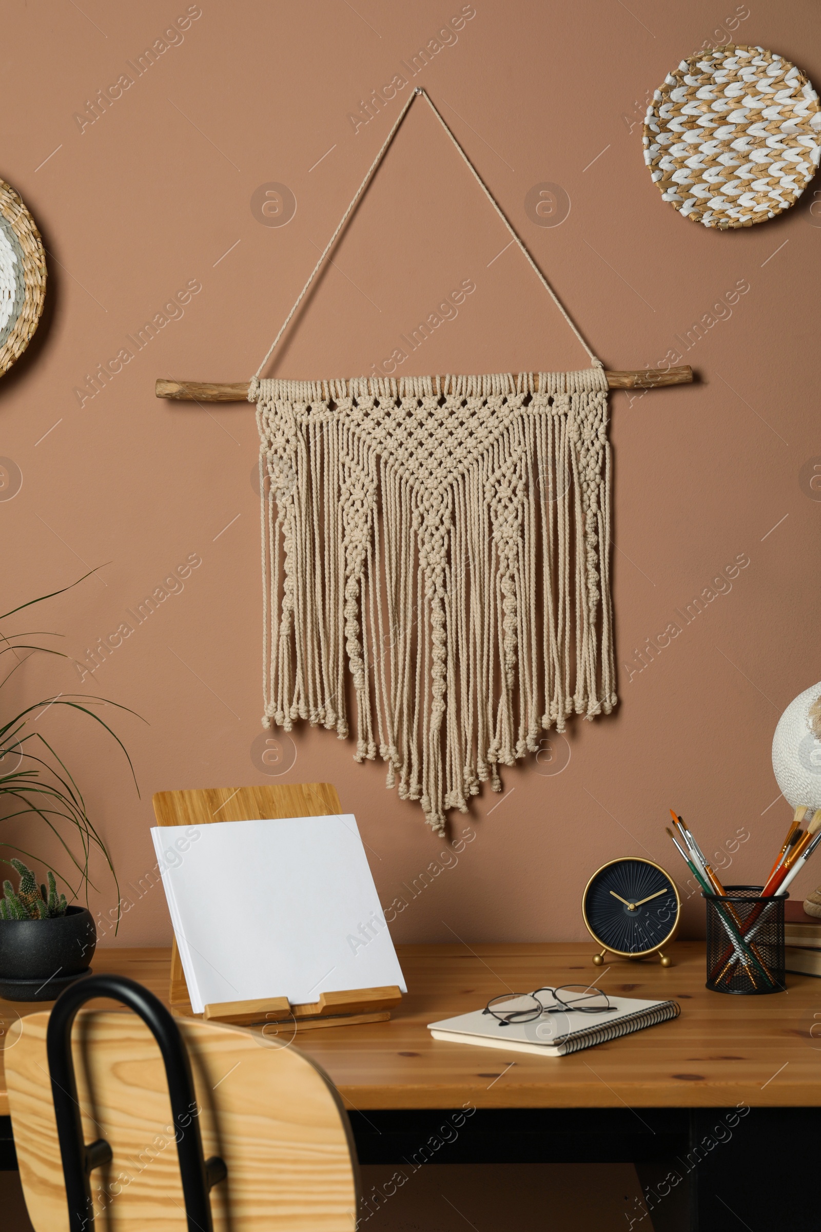 Photo of Stylish macrame and wicker wall decor hanging above wooden table with stationery