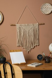 Photo of Stylish macrame and wicker wall decor hanging above wooden table with stationery