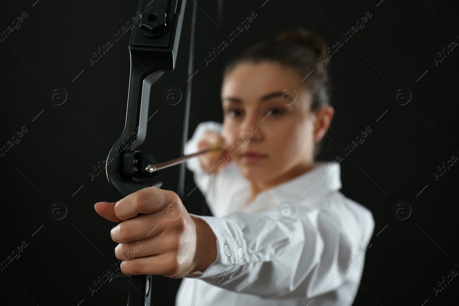 Photo of Businesswoman with bow and arrow practicing archery against black background, focus on hand