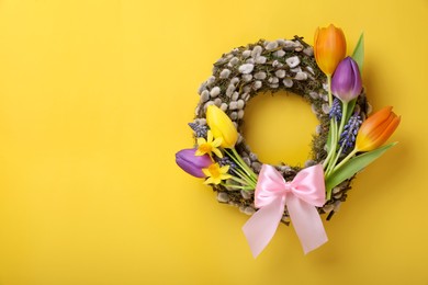 Photo of Willow wreath with different beautiful flowers and pink bow on yellow background, top view. Space for text