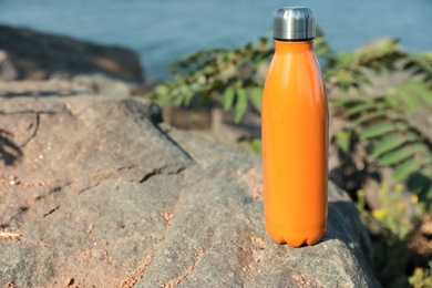 Modern orange thermos on stone near river. Space for text