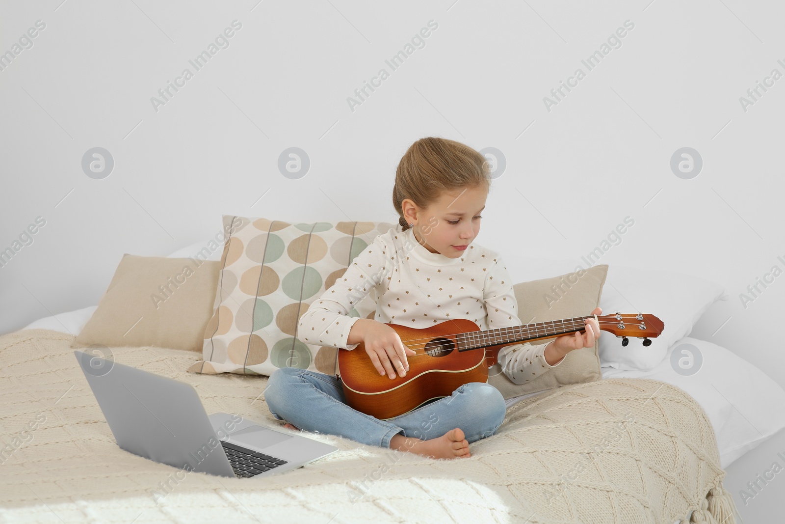 Photo of Little girl learning to play ukulele with online music course at home. Space for text