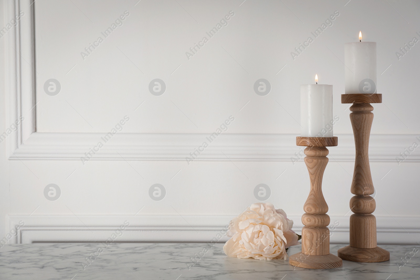 Photo of Elegant candlesticks with burning candles and flower on white marble table. Space for text