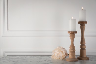 Photo of Elegant candlesticks with burning candles and flower on white marble table. Space for text