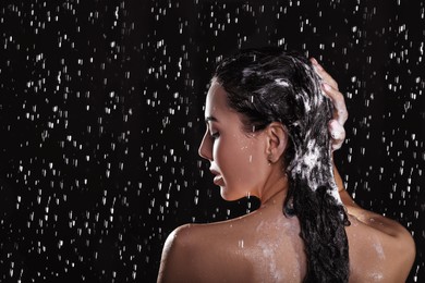 Photo of Young woman washing hair while taking shower on black background