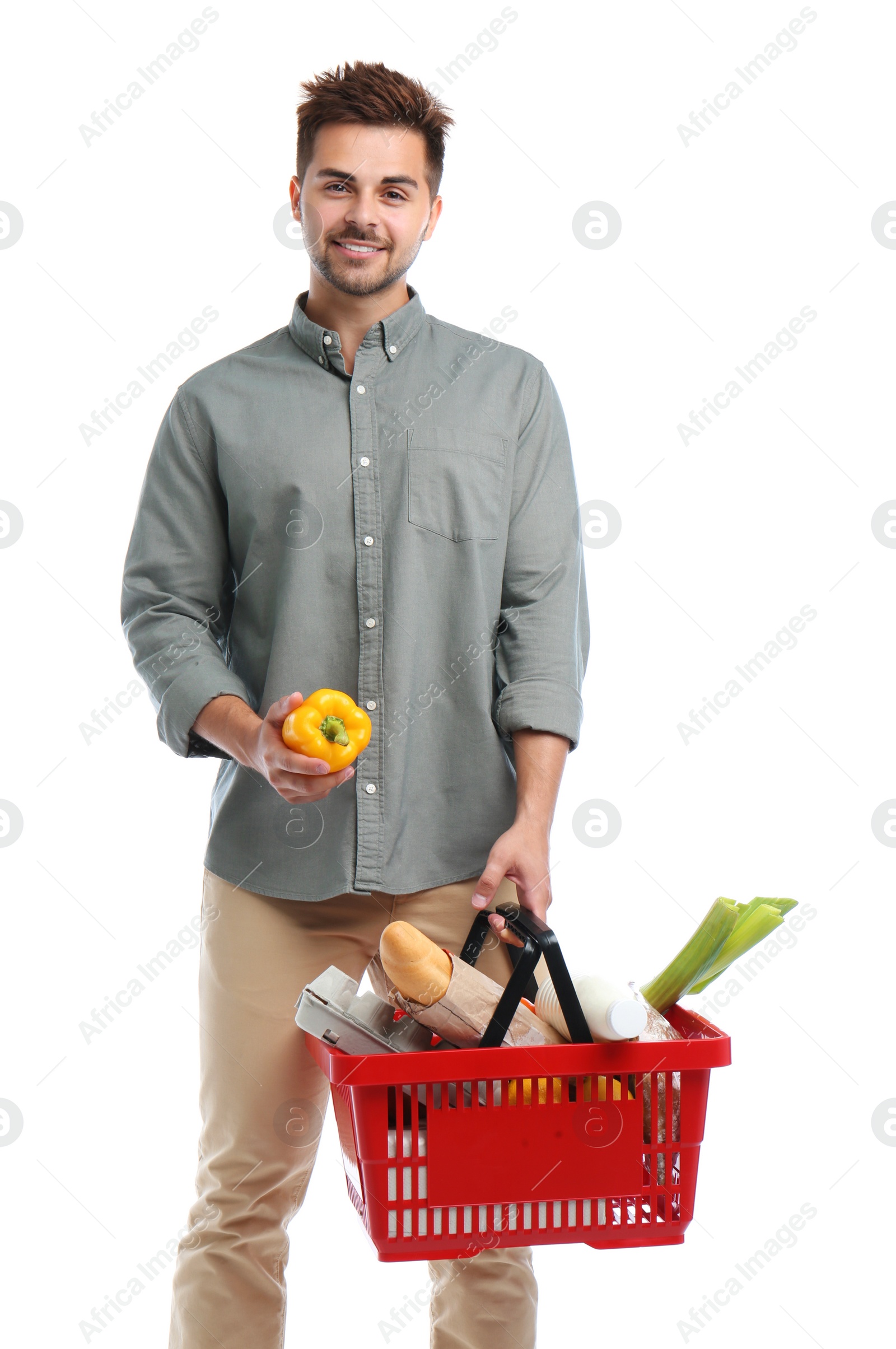 Photo of Young man with bell pepper and shopping basket full of products isolated on white