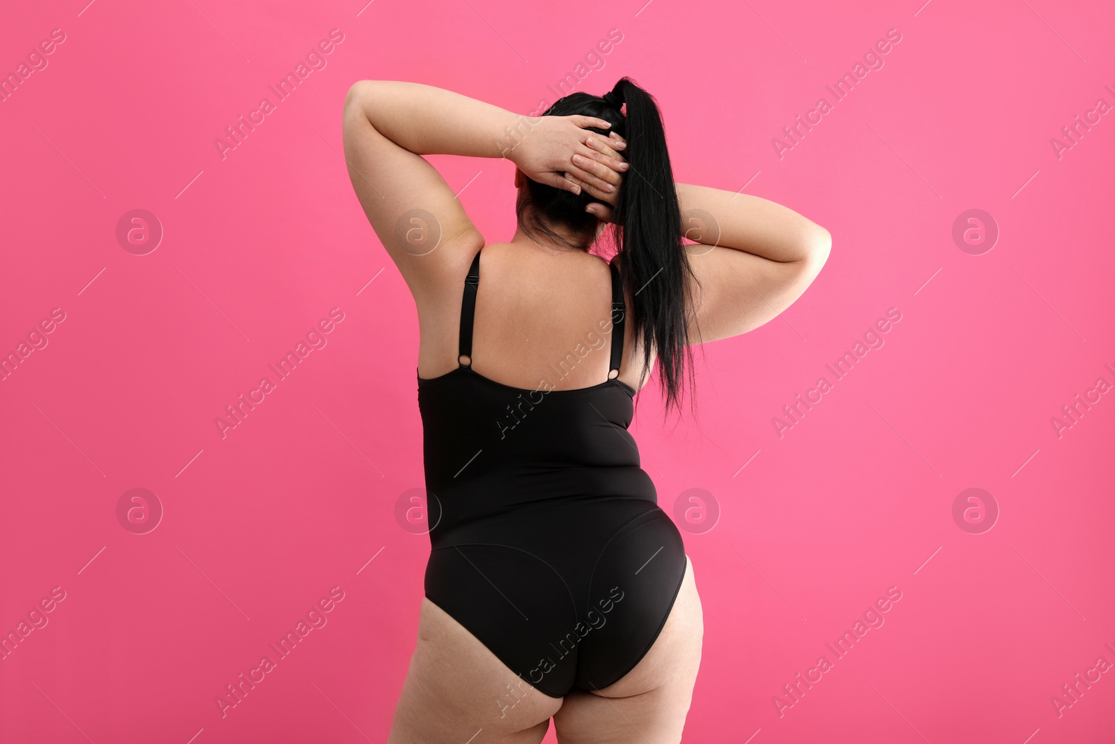 Photo of Back view of overweight woman in black underwear on pink background. Plus-size model