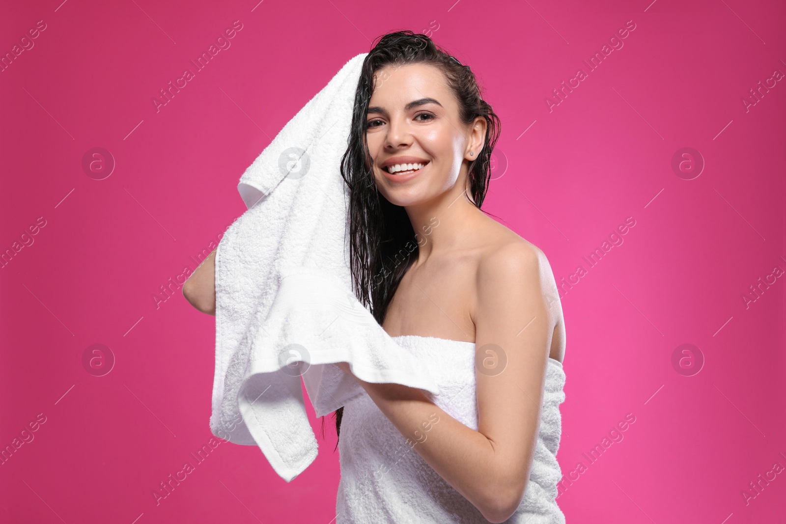 Photo of Happy young woman drying hair with towel after washing on pink background