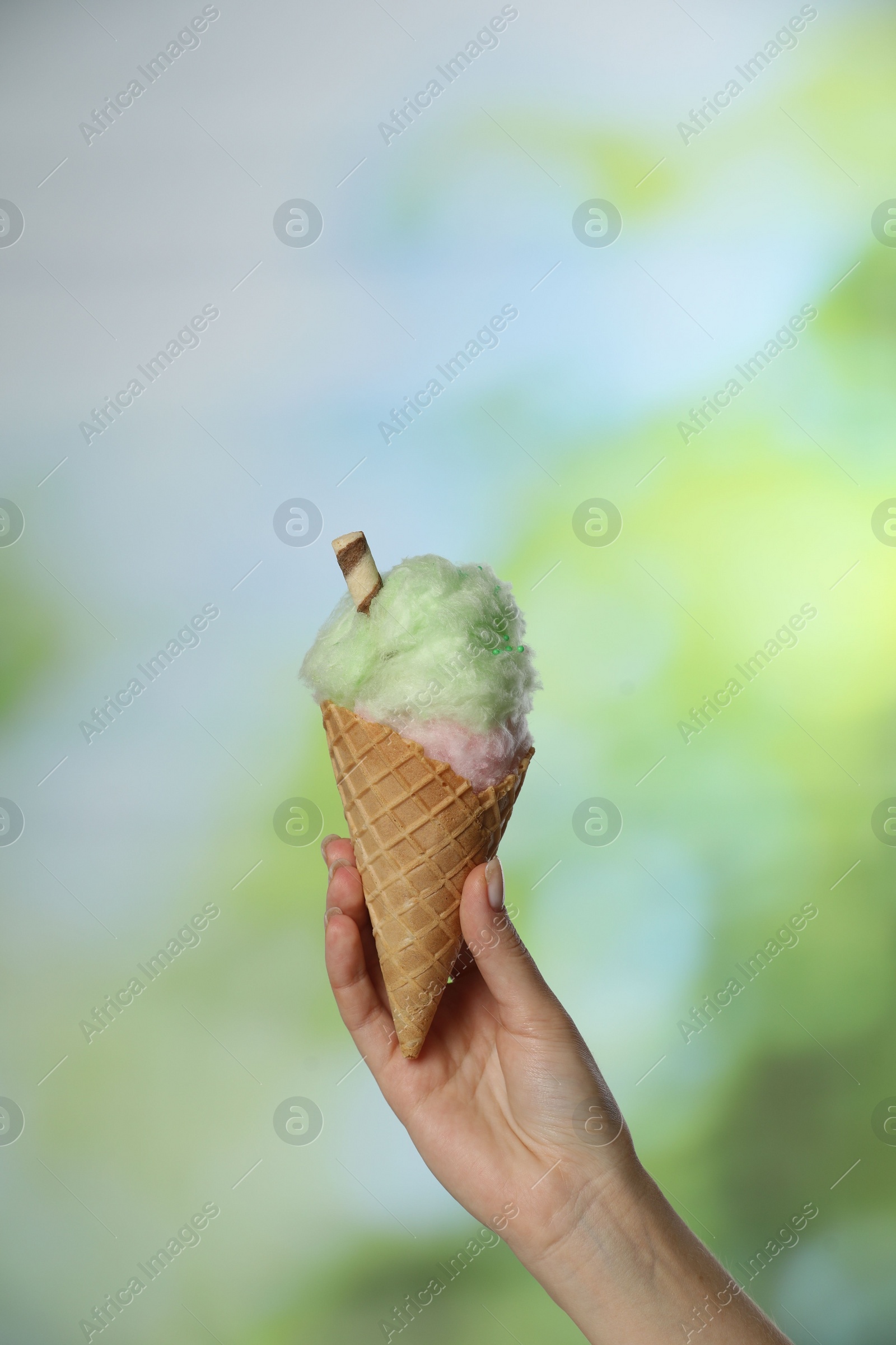 Photo of Woman holding waffle cone with cotton candy on blurred background, closeup