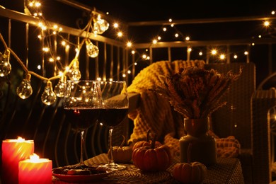 Photo of Glasses of wine, burning candles and decor on rattan table. Autumn evening on terrace