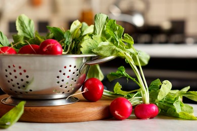 Metal colander with fresh radishes on white table, closeup